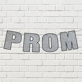 Silver glitter prom streamer banner displayed on a white Brick wall.