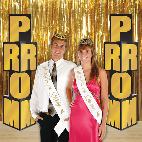 Prom King and Queen with sashes and crowns in front of a gold curtain backdrop with 2 sets of the '"Prom' Decorations