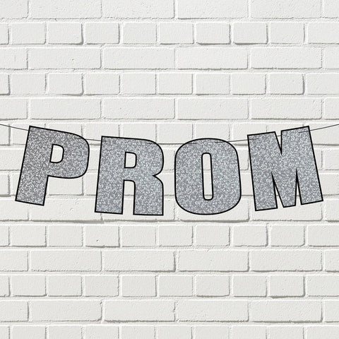 Silver glitter prom streamer banner displayed on a white Brick wall.
